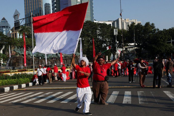 A man waves a large red and white flag at the head of the procession.